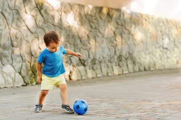 When do babies learn to kick a ball?